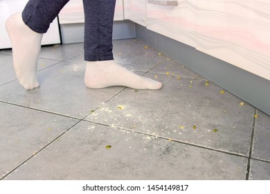 Woman On The Dirty Floor In The Kitchen. Leftovers And Crumbs On The Kitchen Floor. Legs Close-up