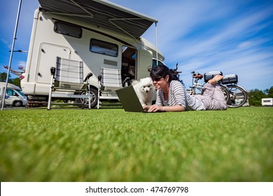 Woman On The Grass With A Dog Looking At A Laptop. Caravan Car Vacation. Family Vacation Travel, Holiday Trip In Motorhome