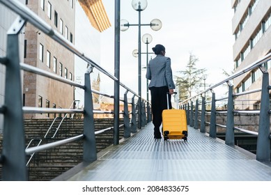 Woman On Her Back With Yellow Suitcase Walking On A Metal Catwalk In The Street. Business Trip Concept.