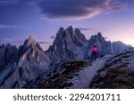 Woman on the hill and mountain peaks at sunset in spring in Dolomites, Italy. Girl on the trail and high rocks at dusk in fall. Colorful landscape with cliffs, stones, purple sky. Trekking and hiking