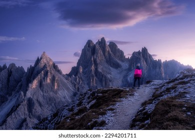 Woman on the hill and mountain peaks at sunset in spring in Dolomites, Italy. Girl on the trail and high rocks at dusk in fall. Colorful landscape with cliffs, stones, purple sky. Trekking and hiking - Powered by Shutterstock