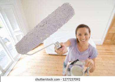 Woman on ladder decorating at home holding paint roller at camera