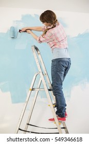 Woman On Ladder Painting Wall With Paint Roller