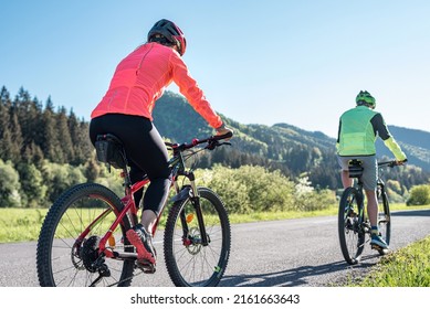 A woman on a mountain bike dressed in a reflective cycling dress rides behind another mountain biker. Visible logos and names was retouched or changed beyond recognition.
