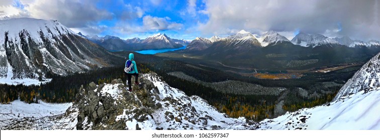 Woman on the mountain top looking at view of snow capped peaks and turquoise lake. Autumn in Canadian Rockies.  Spray lake provincial park. Cananaskis. Canmore. Calgary. Alberta. Canada.