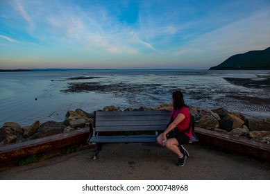 Woman on an outdoor bench looking back at the calm river with sunset in the background