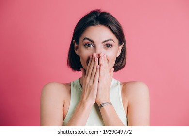 Woman on pink background covering mouth with hands looking at camera, funny excited with unexpected positive surprise