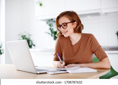 Woman on remote work or online education, using laptop computer, making  notes, indoors at office or home at daytime. Online business, young professional at workplace. Working from home. - Shutterstock ID 1708787632