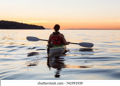 Woman on a sea kayak is paddling in the ocean during a colorful and vibrant sunset. Taken in Jericho, Vancouver, British Columbia, Canada.