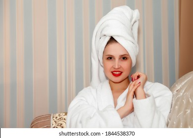 Woman On Sofa Of Hotel Room After Shower. Pretty Female Of Slavic Appearance In Dressing Gown And Towel On Her Head. Happy Lady. Spending Time On Vacation. Cute Girl After Washed And Shows Emotions