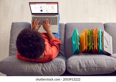 Woman On Sofa Shopping Online, Looking At Laptop PC, Choosing, Buying New Casual Clothes In Internet Outlet Store, Adding Items She Finds To Cart, Paying With Credit Card. Top Overhead View From Above