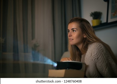 Woman On Sofa Watching Movie Using Digital LCD Video Projector, Home Theater