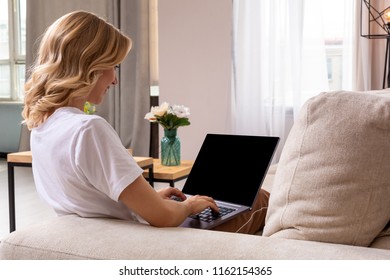 Woman on sofa working on laptop with mockup blank screen. Empty copy space on monitor for advertisement. Black screen.