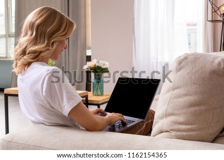Woman on sofa working on laptop with mockup blank screen. Empty copy space on monitor for advertisement. Black screen.