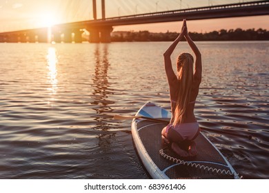 Woman on stand up paddle board. Having fun on SUP board during sunset. Active lifestyle. Yoga practicing.