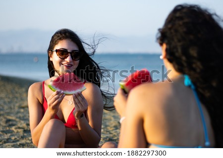 Woman on summer beach vacation enjoying sunny day by the sea, eating watermelon with friend