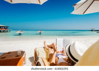 Woman on sunbed reading book under parasol at tropical island
