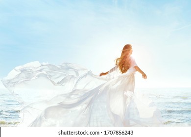 Woman On Sunny Sea Beach In White Fluttering Dress, Fashion Model Back Rear View, Silk Cloth Waving On Wind