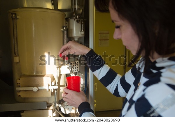 A woman on train carefully pours boiling water into\
a red mug.