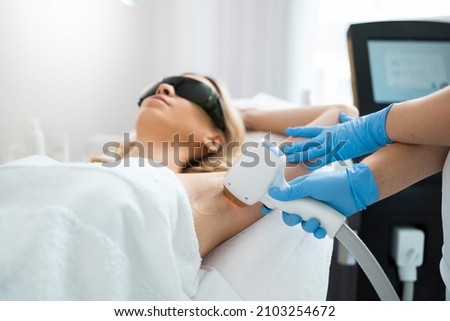 Woman on underarm laser epilation procedure in beauty clinic. Beautician removing hair of pretty blonde armpit