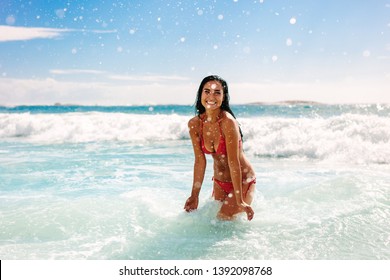 Woman on vacation having fun at the beach playing in the water. Female in bikini enjoying splashing water at the beach.