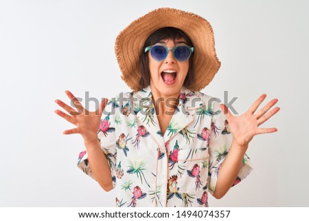 Woman on vacation wearing summer hat shirt and sunglasses over isolated white background very happy and excited, winner expression celebrating victory screaming with big smile and raised hands