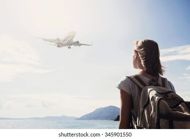 Woman On Vacations. Back Side Of Traveler Girl Looking At The Flying Plane Above The Sea, Travel And Active Lifestyle Concept