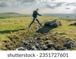 A woman on a walk steps over a small stream in Dartmoor National Park in the UK