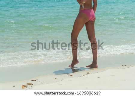 Woman on Whitsundays beach, walking on white sand, in pink bikini & hat, with aqua turquoise ocean. Travel, holiday, vacation, paradise, exotic. Whitsundays Islands, Queenstown, Australia.