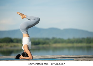 Woman on a yoga mat to relax in the park. Young sporty asian woman practicing yoga, doing headstand exercise, working out, wearing sportswear, pants and top. - Powered by Shutterstock