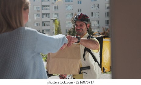 Woman Open Door To A Food Delivery Man On A Bike Wearing Yellow Thermal Backpack And Recieves Order Or Package With Food. Food Delivery Concept.