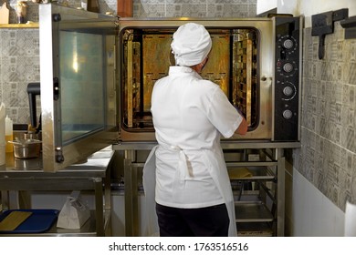 Woman at the open door of a professional oven, metal, glass, shelves, pastries. Cook works in the open kitchen of the restaurant - Powered by Shutterstock