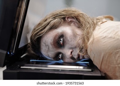 Woman With Open Eyes And Zombie Greasepaint On Face Keeping Her Head On Screen Of Xerox Machine