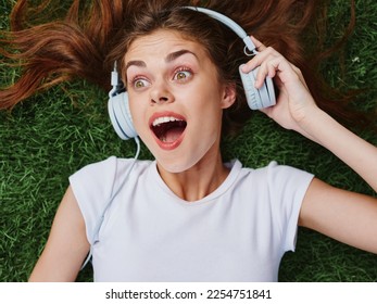 Woman open mouth surprise lying on green grass with headphones spread her hair on the ground in summer - Shutterstock ID 2254751841