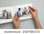 Woman with open photo album and photos on grey background, top view