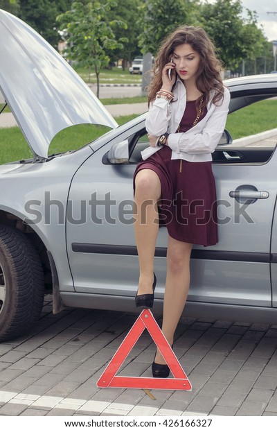 Woman opened hood of the car, she put emergency\
sign and she asks for help by telephone. Concept: a road accident,\
car service