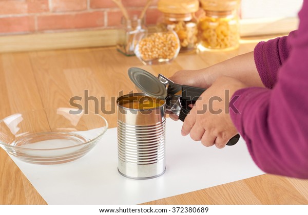 woman opening a can of corn with can opener in\
the kitchen