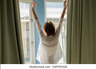 woman opening curtains in the bedroom in the morning