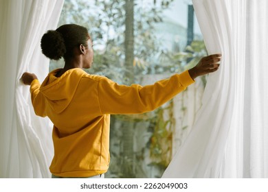 Woman opening curtains in living room to let sunlight in - Powered by Shutterstock