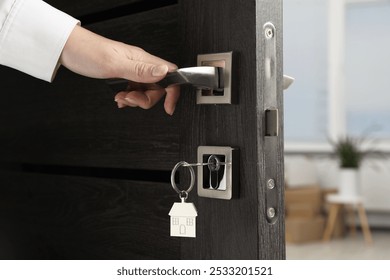 Woman opening door with key and house shaped keychain, closeup