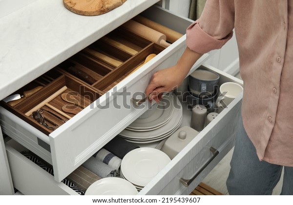 Woman opening drawers of kitchen
cabinet with different dishware and utensils,
closeup