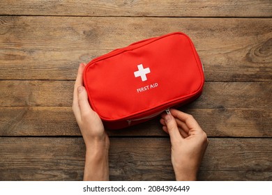 Woman Opening First Aid Kit Bag At Wooden Table, Top View