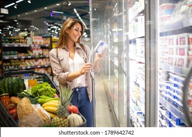 Woman Opening Fridge Door And Taking Food In Supermarket. Buying Food In Grocery Store.