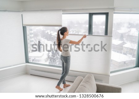 Woman opening home curtains in urban condo. Modern top down bottom up privacy cellular shades on apartment window keeping heat in winter with honeycomb blind curtain. Cordless pleated shades.