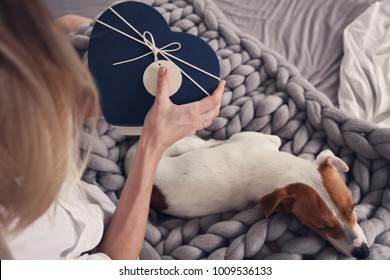 Woman Opening Present Gift Box. Cozy ,lazy Day At Home, Cold Weather, Warm Blanket. Dog Sleeping On Female Feet. Relax, Carefree, Comfort Lifestyle.