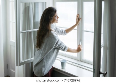 Woman is opening window to look at beautiful snowy landscape outside - Shutterstock ID 748728976