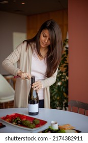 Woman Opens A Bottle Of Wine On A Table With A Lot Of Food