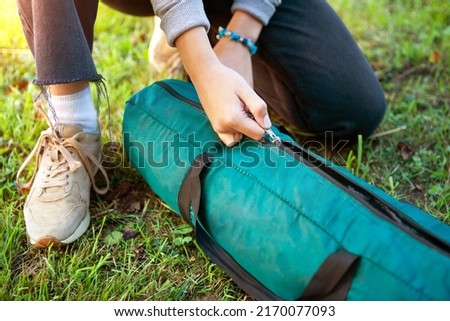 A woman opens a cover with a tent on the grass. Close-up of her hands unzip the zipper. Tourism concept. Trekking and camping.