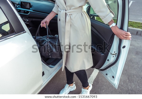 woman opens door\
of business class taxi car, bag in her hand after shopping,\
fashionable modern fashion girl, car sharing rental. In autumn\
summer, parking shopping\
center
