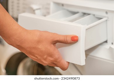 A woman opens the tray for pouring laundry detergent into the washing machine. The concept of washing dirty clothes in a washing machine. Use of various detergents for clothes.